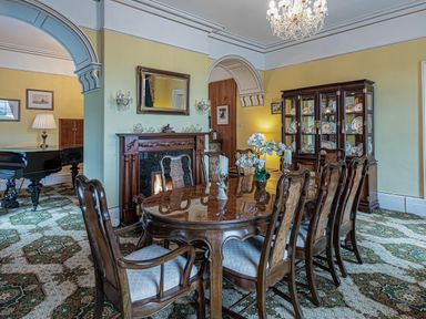 A dining room with a wooden table and chairs a fireplace and a china cabinet at Tal Gwynedd in Dwyran near Newborough