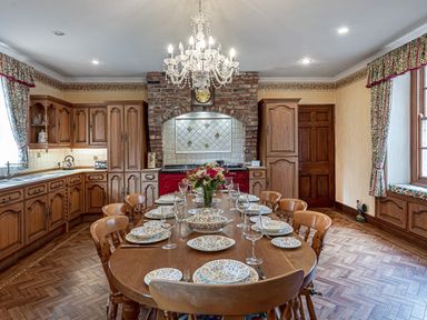 A kitchen with wooden cabinets an oval dining table set with floral plates and glassware at Tal Gwynedd in Dwyran near Newborough