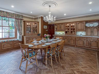 A dining room with a wooden table set with plates and chairs by a window with floral curtains at Tal Gwynedd in Dwyran near Newborough