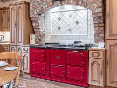 A kitchen with wooden cabinets a red stove and brick arch at Tal Gwynedd in Dwyran near Newborough