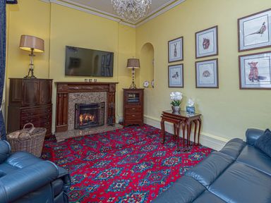 A living room with blue leather sofas a fireplace and animal art on the walls at Tal Gwynedd in Dwyran near Newborough