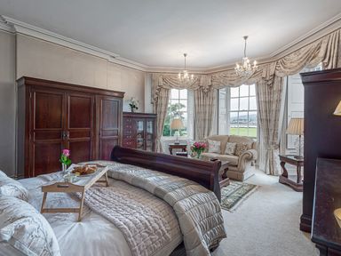 A bedroom with a wooden bed chest of drawers a sofa and large windows at Tal Gwynedd in Dwyran near Newborough