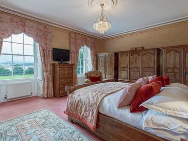 A bedroom with a bed red pillows wooden wardrobes and large windows at Tal Gwynedd in Dwyran near Newborough