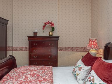 A bedroom with a wooden chest of drawers a bed with red and patterned pillows and a bedside lamp at Tal Gwynedd in Dwyran near Newborough