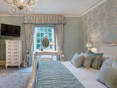 A bedroom with a bed with pillows and a quilt a vanity table with mirror and lamp a chest of drawers and a wall mounted television at Tal Gwynedd in Dwyran near Newborough