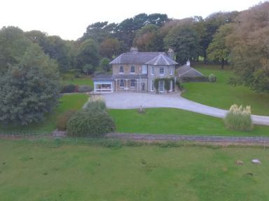 A two-story house with a driveway and surrounding trees at Tal Gwynedd in Dwyran near Newborough