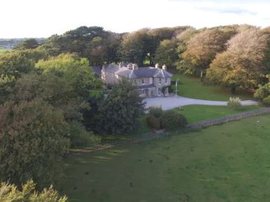 A large house surrounded by trees and a lawn with a curved driveway at Tal Gwynedd in Dwyran near Newborough
