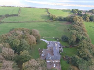 An aerial view of a large house surrounded by trees and green fields at Tal Gwynedd in Dwyran near Newborough
