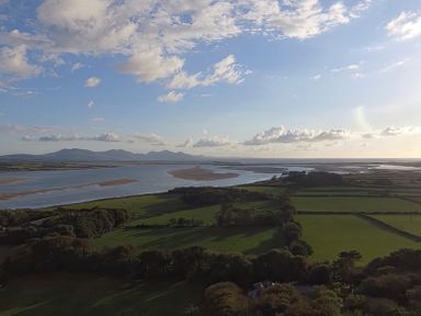 An aerial view of fields with trees and a river flowing towards the ocean with mountains in the distance at Tal Gwynedd in Dwyran near Newborough