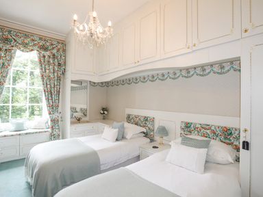 A bedroom with two single beds blue and floral patterned curtains and cushions at Tal Gwynedd in Dwyran near Newborough
