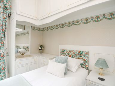 A bedroom with a bed a nightstand with a lamp a sink with a mirror and floral curtains at Tal Gwynedd in Dwyran near Newborough