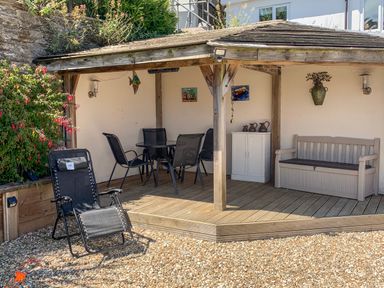 An outdoor covered seating area with a table and chairs a bench and a reclining chair on a gravel patio at Simples in Dartmouth