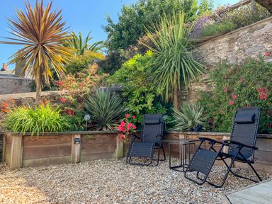 A garden area with two black reclining chairs and plants in raised wooden beds at Simples in Dartmouth