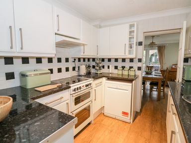 A kitchen with white cabinets black and white checkered backsplash and wooden floor at Heath Cottage in Stratford Upon Avon