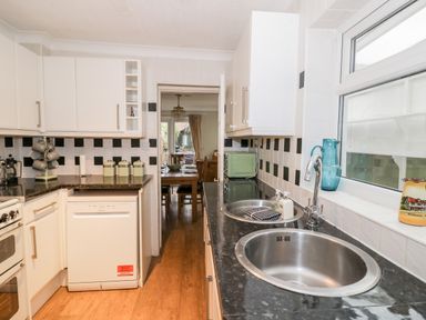 A kitchen with black countertop double sink white cabinets and appliances at Heath Cottage Stratford-Upon-Avon