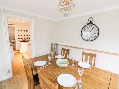 A dining room with a wooden table set with plates and glasses and a clock on the wall at Heath Cottage in Stratford-Upon-Avon