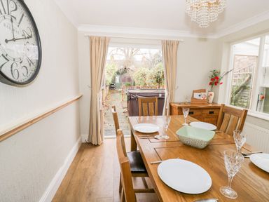 A dining room with a wooden table set with plates and glasses and a large clock on the wall at Heath Cottage in Stratford-Upon-Avon