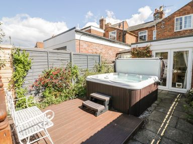 An outdoor patio area with a hot tub wooden steps and a white metal bench at Heath Cottage in Stratford-Upon-Avon