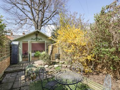 A garden with a table and chairs on a patio near a shed with open doors at Heath Cottage in Stratford-Upon-Avon