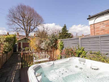 A garden with a hot tub a metal bench a wooden fence and a small green shed at Heath Cottage in Stratford-Upon-Avon