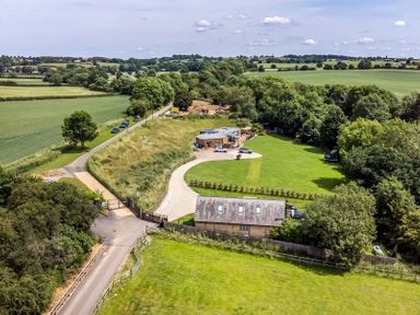 A rural property with a driveway, lawn, and two buildings surrounded by fields and trees at Willow Lodge At Bridge Lake Farm & Fishery in Chacombe