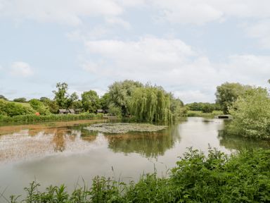 A lake with willow trees and fishing huts at Willow Lodge At Bridge Lake Farm & Fishery Chacombe