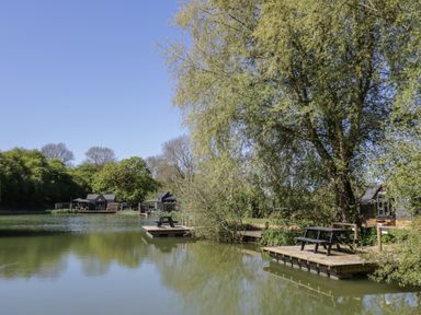 A lake with dock and seating area at Willow Lodge At Bridge Lake Farm & Fishery Chacombe