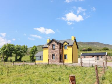 A yellow house with stone accents and a detached stone building in a grassy area at Lack Cottage Annascaul near Camp County Kerry
