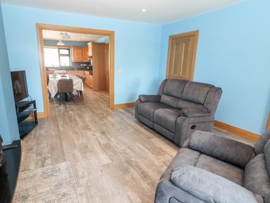 A living room with two gray sofas and a television showing a kitchen and dining area at Lack Cottage in Annascaul near Camp County Kerry