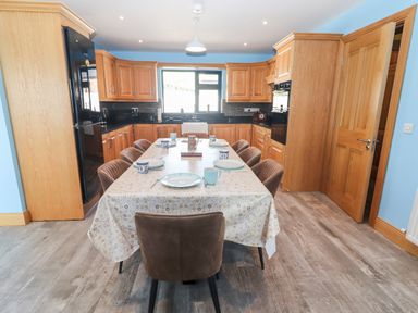 A kitchen with wooden cabinets a dining table set with plates and mugs and brown chairs at Lack Cottage in Annascaul near Camp County Kerry