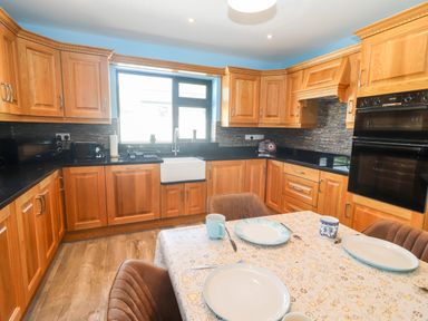 A kitchen with wooden cabinets and black countertops with a dining table set with plates and cups at Lack Cottage Annascaul near Camp County Kerry