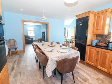 A dining area with a table set for six and brown chairs in a kitchen with wooden cabinets and a black refrigerator at Lack Cottage Annascaul near Camp County Kerry