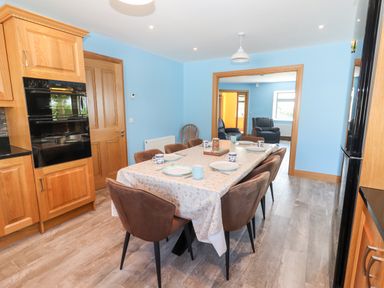 A dining area with a table set for meals and six chairs adjacent to a kitchen at Lack Cottage in Annascaul near Camp County Kerry