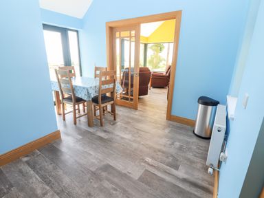 A dining area with a table and four chairs next to glass doors leading to a living room with armchairs at Lack Cottage in Annascaul near Camp County Kerry