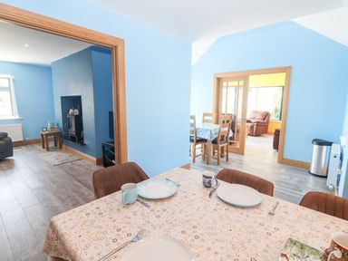 A dining area with a table set for three next to a living room with a fireplace and an adjoining room with chairs at Lack Cottage Annascaul near Camp County Kerry