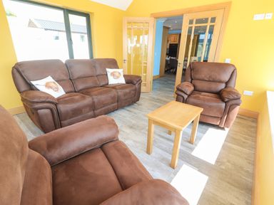 A living room with brown sofas a wooden table and glass doors at Lack Cottage Annascaul near Camp County Kerry