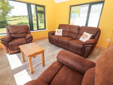 A living room with brown armchairs and sofa with dog print cushions and a wooden table at Lack Cottage in Annascaul near Camp County Kerry
