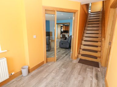 A hallway with wooden stairs and carpet runners and an open glass door leading to a living area at Lack Cottage in Annascaul near Camp County Kerry