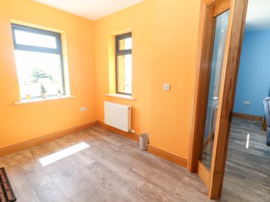 A small empty room with orange walls two windows wooden door and grey floor at Lack Cottage Annascaul near Camp County Kerry