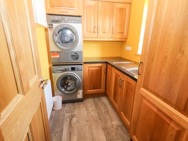A utility room with stacked washer and dryer wooden cabinets and a countertop with a sink at Lack Cottage Annascaul near Camp County Kerry
