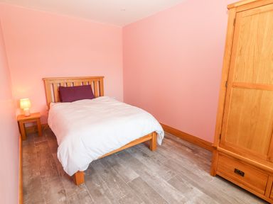 A bedroom with a wooden bed frame white bedding a purple pillow a wooden nightstand with a lamp and a wooden wardrobe at Lack Cottage Annascaul near Camp County Kerry
