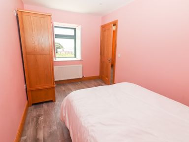 A bedroom with pink walls a bed a wooden wardrobe a window and a wooden door at Lack Cottage in Annascaul near Camp County Kerry