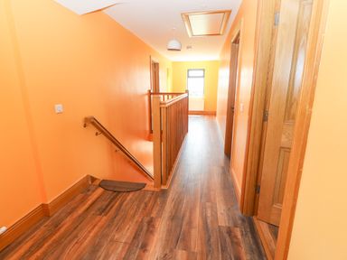 A hallway with wooden floor and orange walls with a staircase and open doors at Lack Cottage Annascaul near Camp County Kerry