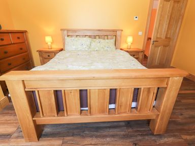 A bedroom with a wooden bed frame two bedside tables with lamps and a wooden dresser at Lack Cottage in Annascaul near Camp County Kerry