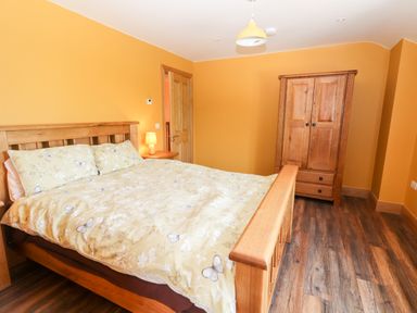 A bedroom with a wooden bed, nightstand with lamp, wooden wardrobe, and wooden flooring at Lack Cottage in Annascaul near Camp County Kerry