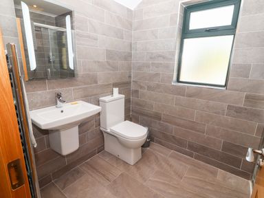 A bathroom with a wall-mounted sink a toilet a mirror and a window at Lack Cottage in Annascaul near Camp County Kerry
