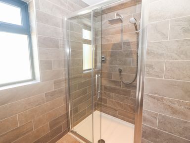 A shower enclosure with glass doors and tiled walls with a window at Lack Cottage in Annascaul near Camp County Kerry