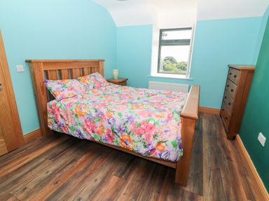 A bedroom with a wooden bed and floral bedding wooden dresser and nightstand with lamp at Lack Cottage Annascaul near Camp County Kerry
