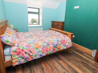 A bedroom with a wooden bed with floral bedding a wooden dresser and a window at Lack Cottage Annascaul near Camp County Kerry