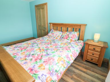 A bedroom with a wooden bed and nightstand with a lamp and floral bedding at Lack Cottage in Annascaul near Camp County Kerry